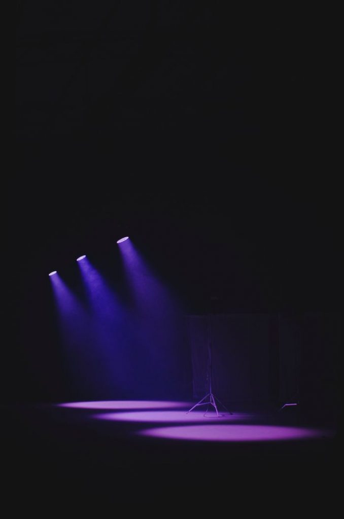 Moody theater scene with purple spotlights casting a vivid glow on an empty stage.