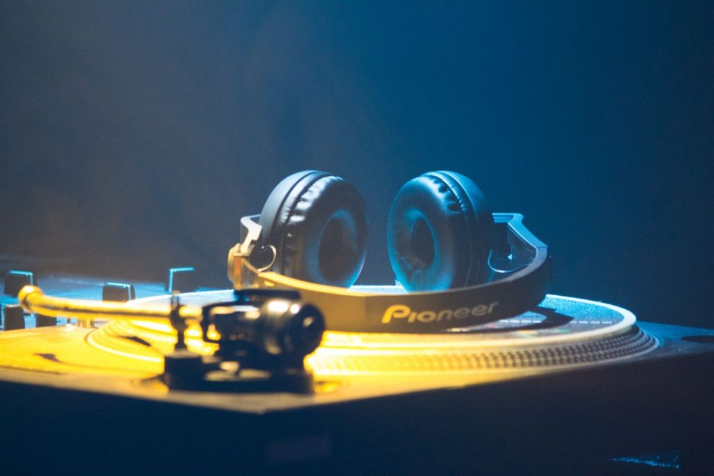Contemporary headset on platter disc of music controller with knobs and faders in yellow neon light on blue background