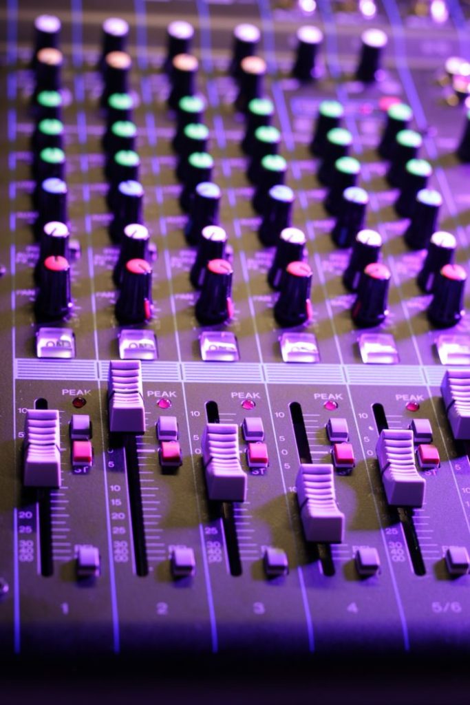 Vertical close-up of an audio mixer with vibrant knobs and sliders. Ideal for music tech themes.